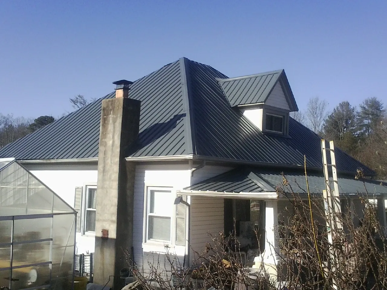 Dark blue standing seam metal roof on a white farmhouse with dormer — Slate & Tile Roof Repair by Roofing Brothers in Munson