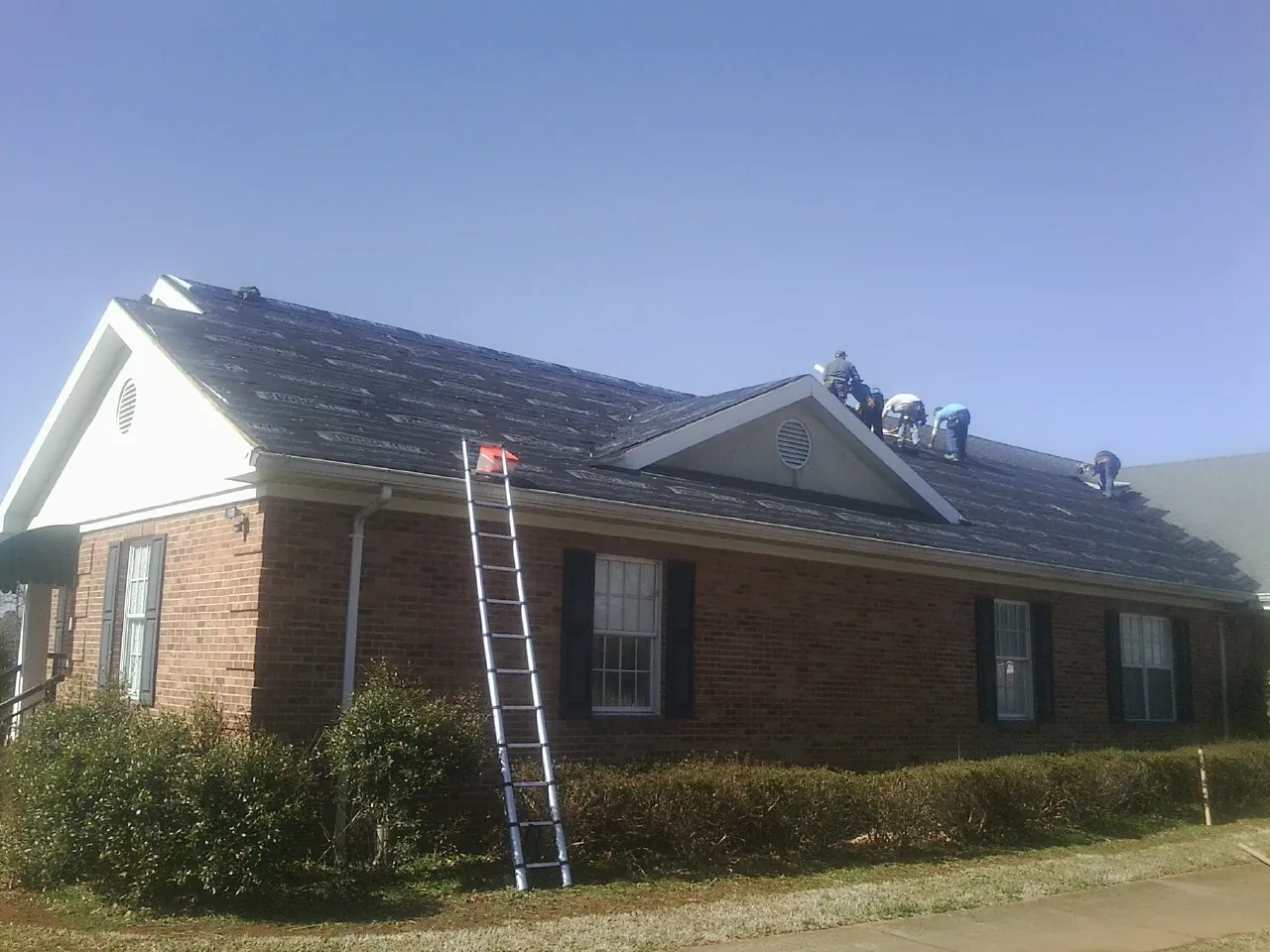 Crew tearing shingles off a brick ranch roof with a ladder set — Emergency Roof Repair work by our crew in Munson