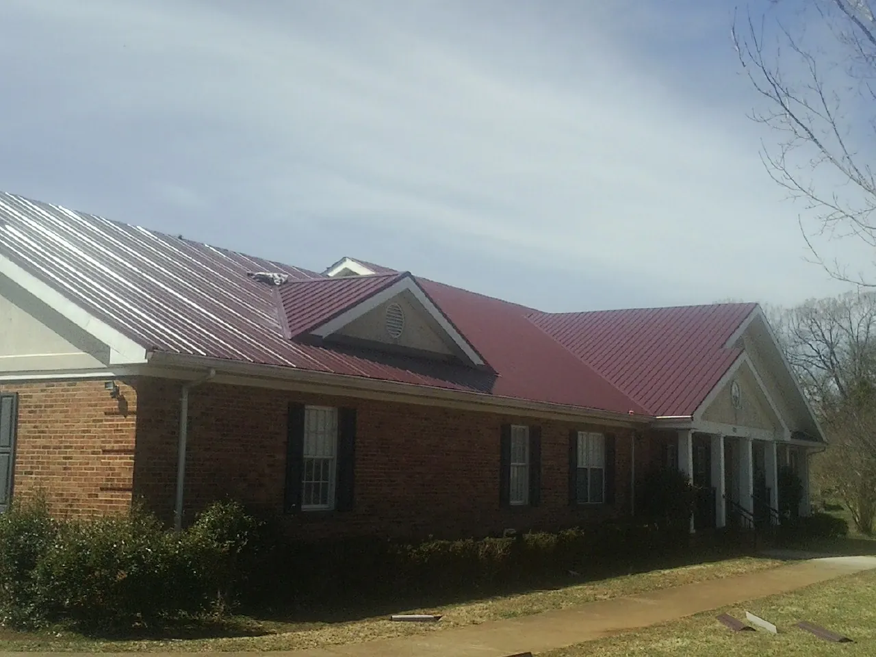 Red metal roof with gabled entries on a long brick building, from a Hail Damage Roof Repair job in Munson
