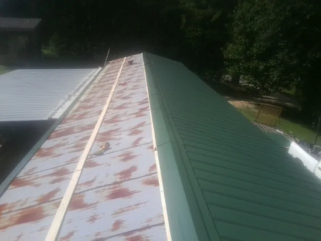 Old rusted panels beside newly installed green metal roofing — Wind Damage Roof Repair by Roofing Brothers in Munson