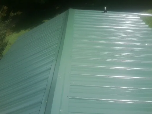 New green metal panels meeting at the ridge of a roof — Flat Roof Repair work by our crew in Munson
