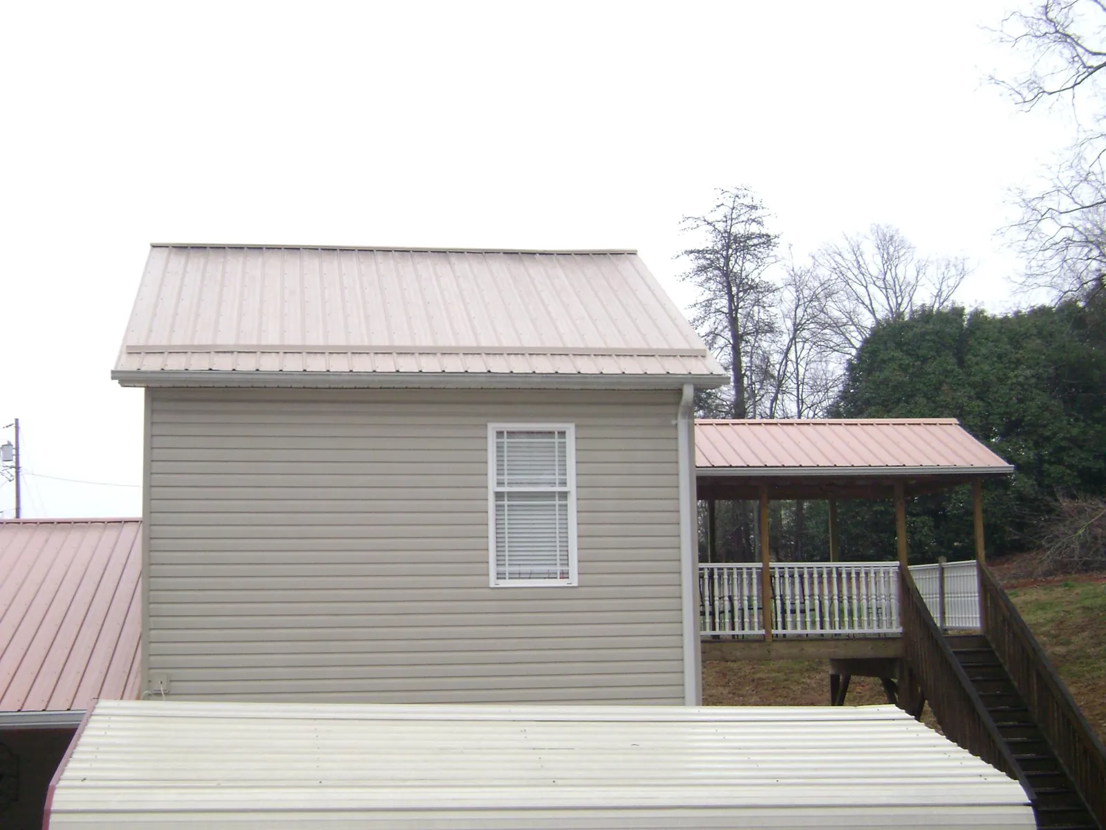 Tan metal roofs on a two story addition and attached porch, from a Roof Replacement job in Munson